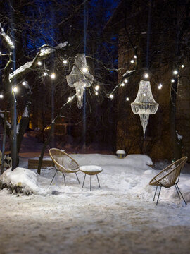 A summer courtyard, buried in snow on a winter evening: a cozy nook with swings, a slide, and benches, completely covered in fresh snow under the warm glow of streetlights. Gray multi-story buildings 
