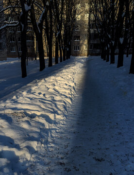 A winter city courtyard with gray multi-story panel buildings (Khrushchev-era or Brezhnev-era buildings) covered in a thin layer of snow and frost, under a bright blue sky