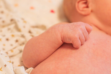 Close-up of a newborn baby's hand resting on soft fabric. The skin is light and smooth, showcasing tiny fingers and a delicate grip.