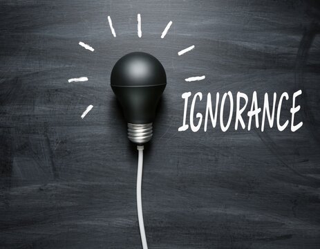 Black light bulb with rays on chalkboard next to word ignorance