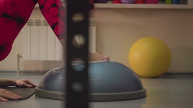 athlete performing single leg lunge on bosu, foot pressing dome, dynamic balance challenge, forward knee alignment, gym equipment in background, yellow exercise ball, intense tempo