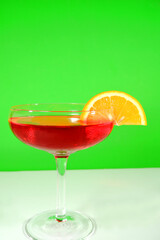 Vibrant close up shot featuring a bright red cocktail garnished with a fresh, juicy orange citrus slice against a vivid green screen background for easy editing.