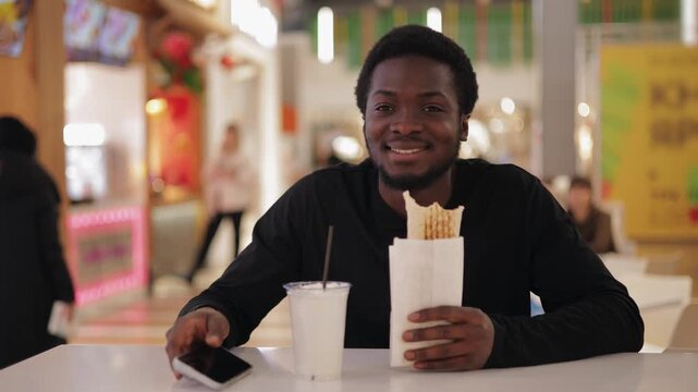 Portrait Young african male eating fast food shawarma at food court in mall shop.