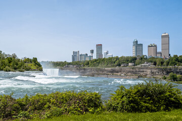 Panoramic view of the powerful Niagara Falls with city skyline and Skylon Tower under blue sky