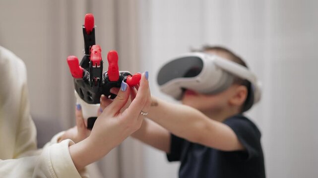 Child playing with vr headset and futuristic toy robotic arm made by 3D printer indoors living room.