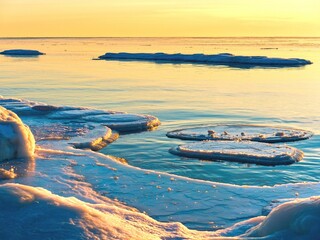 Drifting sea ice and broken ice floes on calm water at golden sunset. Cold winter seascape with natural light, reflections and copy space. © Igor