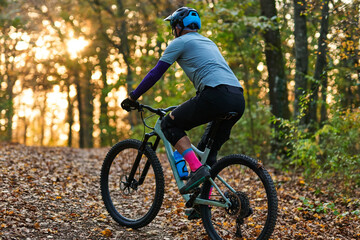 Obraz premium Mountain Biker Riding Through Autumn Forest Trail at Sunset with Sunlit Leaves