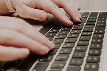 Close-up of female hands typing on a modern laptop keyboard in a home office.