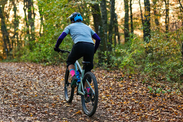 Fototapeta premium Autumn Forest Bicycle Ride: Mountain Bike Rider on Leaf-Covered Trail in Dappled Sunlight
