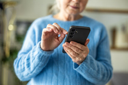 Senior woman using mobile phone at home, closeup of hands
