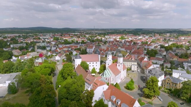 View over the UNESCO World Heritage old town of Bamberg. The characteristic red tiled roofs and historic streets stretch out in front of the forested hills of the Steigerwald under a clear spring sky.