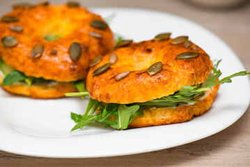 Bagels with cream cheese, fish, pumpkin seeds and arugula in plate, closeup.