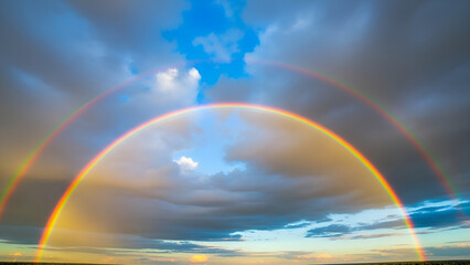 Vibrant double rainbow appears in cloudy sky at sunset with warm sunlight