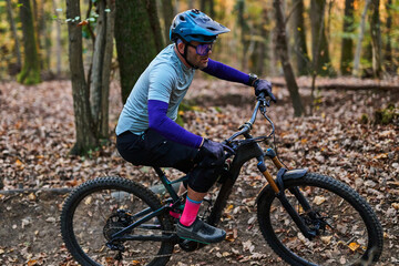 Obraz premium Mountain Biker in Forest Trail Wearing Helmet and Protective Gear During Autumn Ride