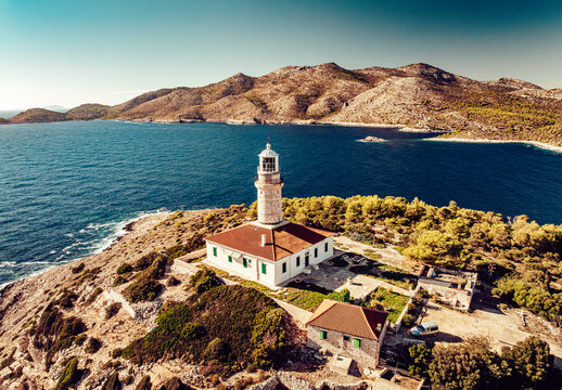 Aerial view of a lighthouse with a red roof standing tall on a rocky promontory, embraced by the deep blue sea and sun-kissed hills, Lastovo, Dubrovnik-Neretva County, Croatia.