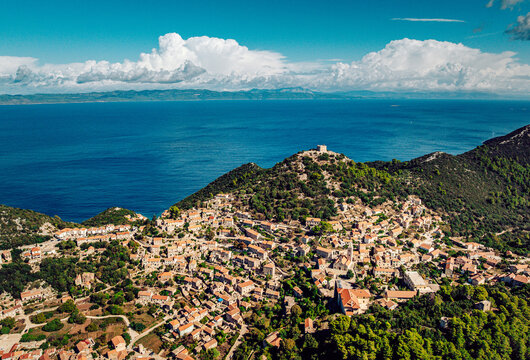 Aerial view of terracotta rooftops cascading down the verdant hillside towards the azure sea, a fortress crowning the peak, Lastovo, Dubrovnik-Neretva County, Croatia.