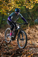 Fototapeta premium Mountain Biker Navigates Leafy Autumn Trail in Forest, Wearing Helmet and Protective Gear