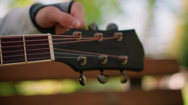white hand adjusting guitar tuning peg outdoors in park, closeup headstock and fretboard, sunlight filtering through leaves, glovecovered wrist, musician prepping for gig, focus on precision