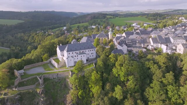 Spectacular aerial view of Wolkenstein Castle, perched on a steep rocky outcrop above the Zschopau Valley. The image shows the striking white castle complex and the adjacent town of Wolkenstein.