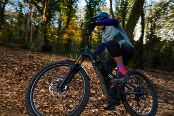 Fototapeta premium Mountain Biker Racing Through Autumn Forest Trail In Action With Helmet And Gear