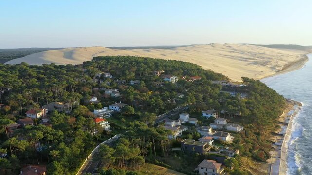 Panorama of the French Atlantic coast near Arcachon. In the foreground, a wooded coastline with exclusive villas stretches out, while the massive silhouette of the Dune du Pilat rises on the horizon.