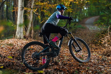 Obraz premium Mountain Biker Navigates Leafy Autumn Trail On Rough Forest Path At Dusk