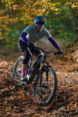 Obraz premium Autumn Mountain Biker In Protective Gear Rides Through Leafy Forest Trail On Rough Path