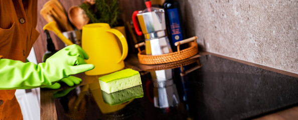 Cleaning woman in green rubber gloves scrubbing induction cooktop sponge in kitchen. Housewife professional maintenance domestic lifestyle appliance housekeeping concept