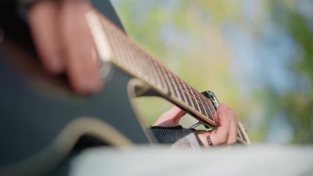 closeup black guitarist fingerpicking acoustic guitar, intimate outdoor park practice with soft bokeh, sunlight on fretboard, denim sleeve and bracelet, mellow chord progressions, reflective