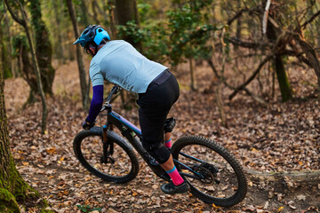 Fototapeta premium Mountain Biker Navigates Forest Trail in Autumn, Wearing Helmet and Bright Gear On Trail Today