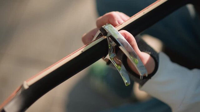 closeup acoustic guitar neck capo placed on fretboard, hand adjusting capo during outdoor practice session, warm sunlight on wooden grain, shallow depth of field, lofi intimate atmosphere