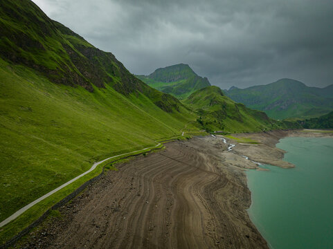 Aerial view of the stark contrast between the dark, textured shoreline and vibrant green hills under a brooding sky, Ritom lake, Quinto, Ticino, Switzerland.