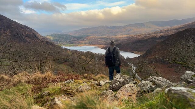 Hiker with Backpack overlooking Llyn Dinas Lake and Mountains in Snowdonia National Park, Gwynedd, Wales, United Kingdom