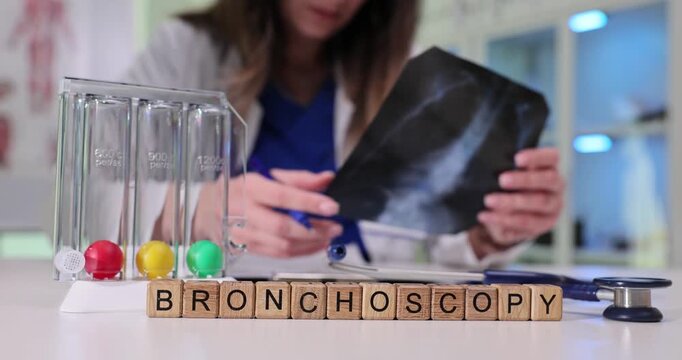 Word Bronchoscopy on wooden cubes near breathing exerciser and stethoscope in clinic. Woman doctor examines patient lungs x-ray image in hospital