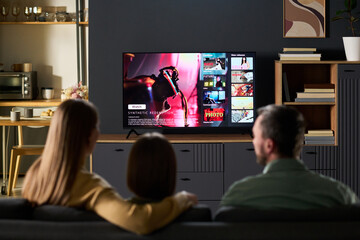 Caucasian couple and their child sitting on sofa watching television together, viewing streaming...