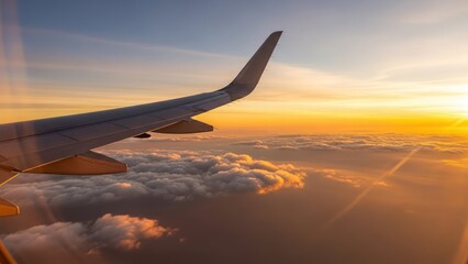 Obraz premium A passenger airplane wing soars above soft clouds, bathed in the vibrant golden glow of sunrise or sunset