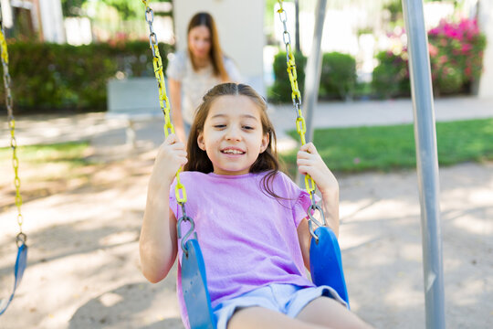 Happy girl smiling while playing on a swing, enjoying childhood fun with mother pushing in park playground
