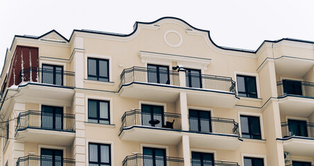 Obraz premium A multi-story residential building with cream-colored facade, ornate balconies with wrought iron railings, and elegant architectural details. Winter setting, subtle snow on balconies.