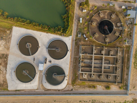 Aerial view of geometric water treatment plant's circular tanks contrasting with the adjacent pond's natural curves, Kraaifontein, Western Province, South Africa.