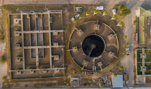 Aerial view of a treatment facility with geometric tanks and structures under the sunlight, creating a stark contrast of shadows and light, Kraaifontein, Western Province, South Africa.