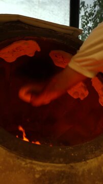 Flatbread sticks to the wall of a glowing taboon oven as a baker presses dough, vertical handheld close up