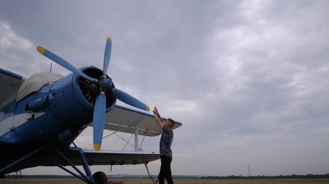 Pilot inspecting vintage blue biplane, engaging with propeller and engine components, showcasing pre-flight preparations and attention to detail in aviation maintenance