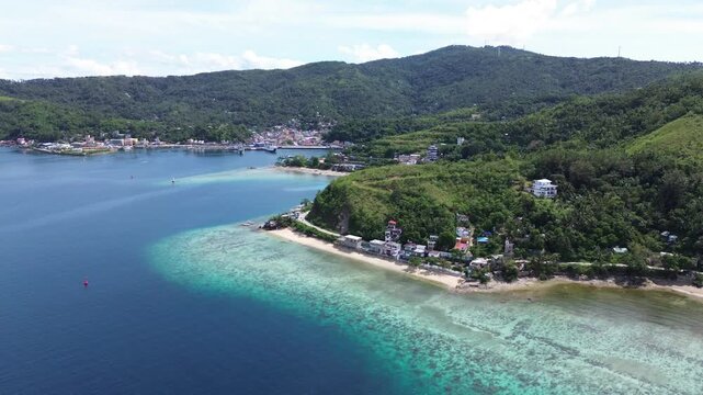 Cinematic aerial view of Romblon town and port in Romblon Philippines showing turquoise bay coastal houses beach and green hills under a clear blue sky on a sunny tropical day captured in 4K