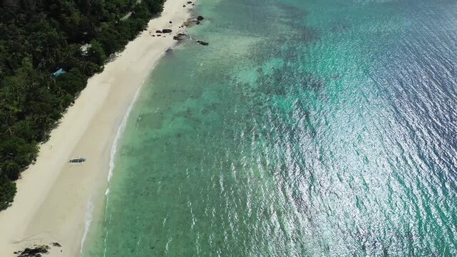 Cinematic aerial view of Tiamban Beach in Romblon Philippines showing turquoise ocean white sand shoreline and lush green hills in the background under a clear blue sky on a sunny tropical day