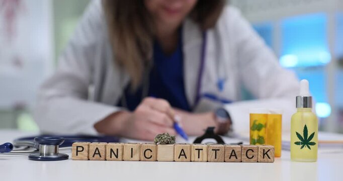 Wooden cubes spell phrase Panic Attack near cannabis oil bottle. Woman doctor writes note about panic disorder symptoms during medical visit