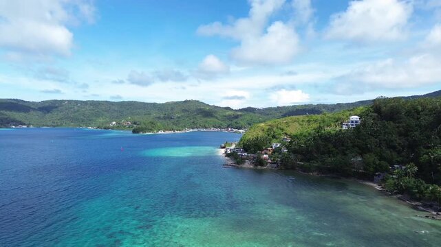 Cinematic aerial view of Romblon town and port in Romblon Philippines showing turquoise bay coastal houses beach and green hills under a clear blue sky on a sunny tropical day captured in 4K