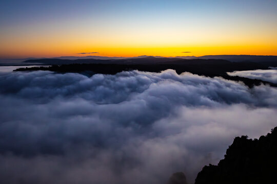 Aerial view of a sea of fog blanketing the landscape under a vibrant sunrise, where dark silhouettes of distant hills meet the sky, Canyon du Sil, Lugo, Spain.