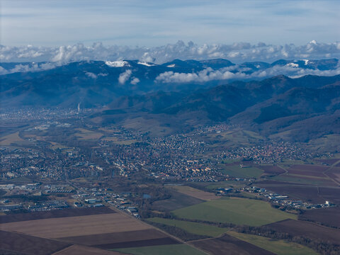 Aerial view of the patchwork fields meet the foothills, blending into the distant, snow-capped mountains under a sky brushed with wispy clouds, Wittelsheim, Grand Est, France.
