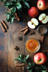 Overhead view of a jar of spiced apple butter next to fresh apples, cinnamon sticks, and cloves, rustic kitchen table