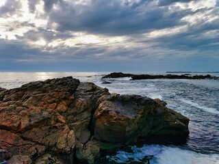 Rocks on the shore of a beach on the coast with clouds in the sky, using long exposure. Seashore with misty water at sunset. Cambria shore. Sea and rocks. Early sunset at a rocky beach.